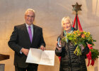Innenminister Joachim Herrmann neben Rosa Carstens mit Blumenstrauß und Ehrenzeichen für ehrenamtliches kirchliches Engagement