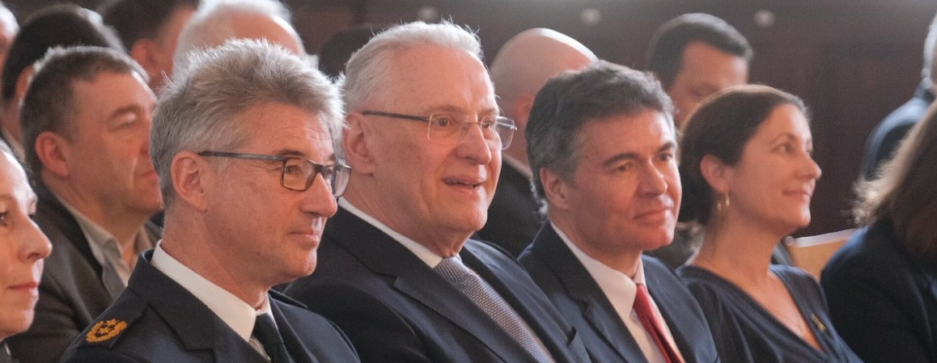 Auf dem Bild ist Innenminister Joachim Herrmann im Publikum sitzend zu sehen, neben ihm sitzen der neue Polizeipräsident Frank Hellwig und dessen Vorgänger, der Präsident des Landesamts für Verfassungsschutz, Manfred Hauser.