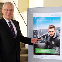 Verkehrsminister Joachim Herrmann zeigt auf das Plakat zur Aktion "Keine Ablenkung im Straßenverkehr" mit Joshua Kimmich